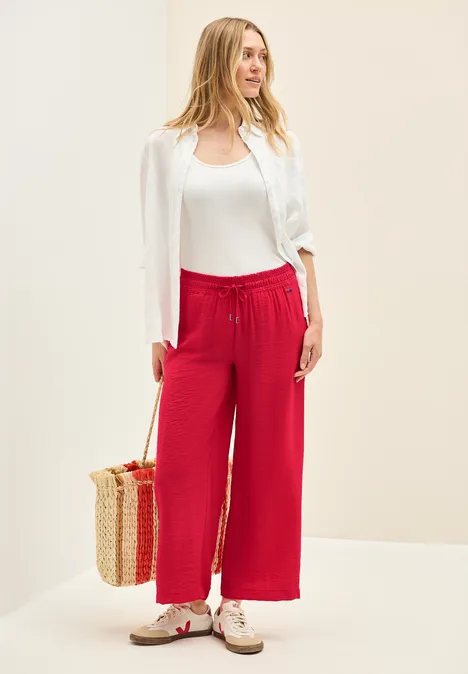 Frau mit weißer Bluse, rotem Hose, Korbtasche und Sneakers.